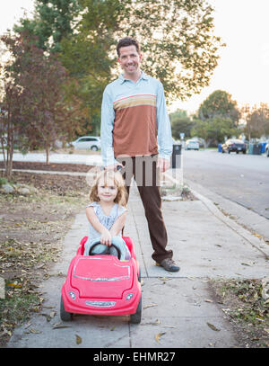 Kaukasische Vater schob Tochter in Spielzeugauto Stockfoto
