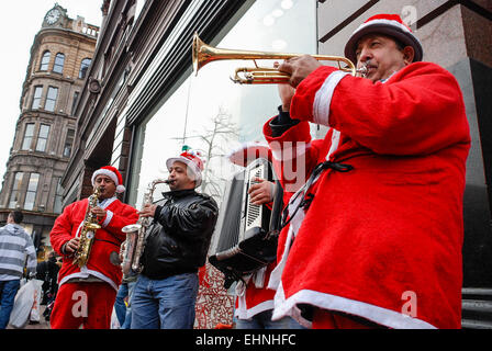 Musiker spielen Weihnachtsmusik auf einer Straße in Belfast als Straßenmusikant Geld während in Santa-Outfits gekleidet Stockfoto