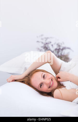 Frau im Bett, Kopf auf Kissen, lächelnd in die Kamera Stockfoto