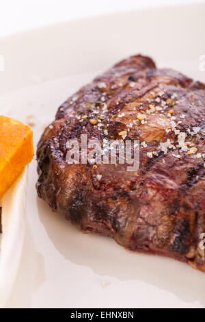 Lecker gegrilltes Rindersteak mit einem gezwirbelten Stück Butter und ein Zweig frischer Rosmarin garniert und serviert auf einem weißen Teller, enge u Stockfoto