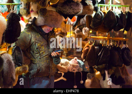 Ein Pelz Hut Verkäufer überprüft sein Telefon auf einem Weihnachtsmarkt in Budapest, Ungarn Stockfoto