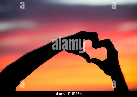 Herz Hände Geste bei Sonnenaufgang. Silhouette Stockfoto