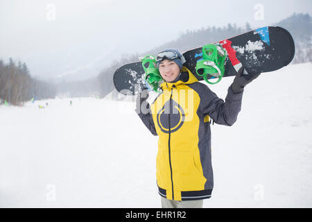 Junger Mann mit Snowboard auf dem Schnee Stockfoto