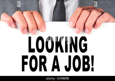 ein Mann in einem Anzug hält ein Schild mit dem Text auf der Suche nach einen Job auf sie geschrieben Stockfoto