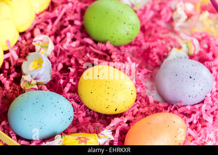 farbige Ostereier, gelben Küken und Süßigkeiten in einem Korb Stockfoto