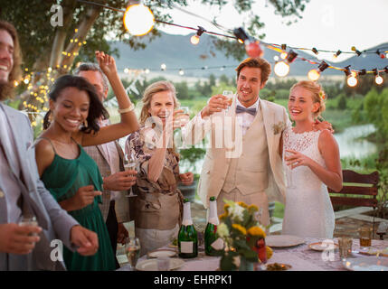 Junge Paare und Gäste Toasten mit Champagner während der Hochzeitsfeier im heimischen Garten Stockfoto
