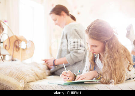 Zwei Mädchen im Teenageralter auf Bett schriftlich Notizblöcke Stockfoto