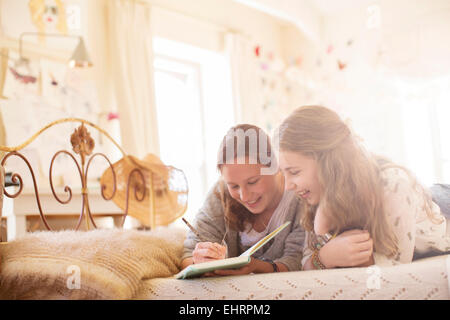 Zwei Mädchen im Teenageralter auf Bett liegend und schreiben in notebook Stockfoto