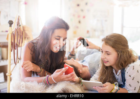 Drei Mädchen im Teenageralter Verwendung elektronischer Geräte während auf Bett liegend Stockfoto
