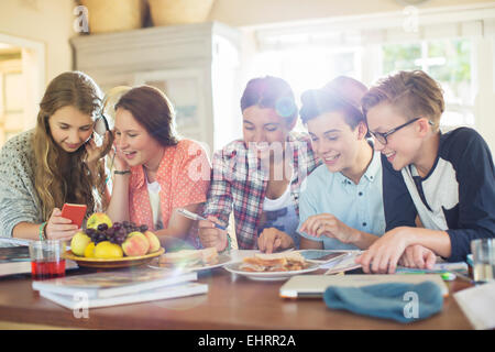 Gruppe von Jugendlichen, die Verwendung elektronischer Geräte am Tisch im Speisesaal Stockfoto