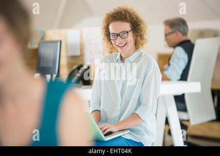 Porträt Frau mit Laptop und lachen, Mann, arbeitet im Hintergrund Stockfoto