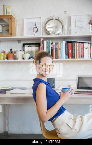 Junge Frau sitzt mit Becher im home-office Stockfoto