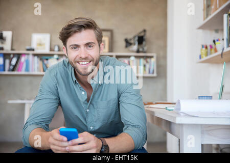 Porträt der junge blonde Mann, sitzend mit Mobiltelefon Stockfoto