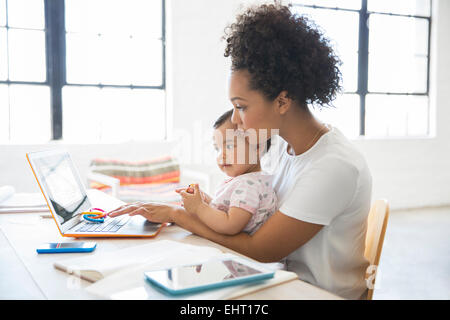 Mutter mit Tochter sitzt auf dem Schoß von zu Hause aus arbeiten Stockfoto