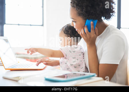 Mutter mit Tochter sitzt auf dem Schoß von zu Hause aus arbeiten Stockfoto