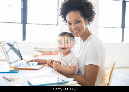 Mutter mit Tochter sitzt auf dem Schoß von zu Hause aus arbeiten Stockfoto