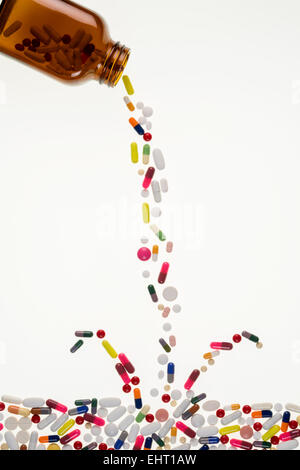 Medikamente aus einer Medizin-Flasche gießen und Spritzwasser in ein Meer von Tabletten, Pillen und Kapseln. Stockfoto