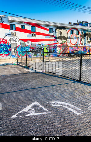 Pfeil auf Bürgersteig auf einem Parkplatz und Graffiti an einem Gebäude in Baltimore, Maryland. Stockfoto