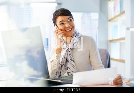 Weibliche Büroangestellte sitzen am Schreibtisch mit Smartphone, arbeiten Stockfoto