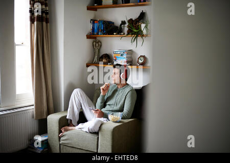 Mann sitzt im Sessel mit Kopfhörern Blick durch Fenster Stockfoto