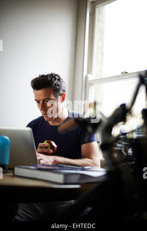 Mann arbeitet am Laptop zu Hause essen Apfel Stockfoto