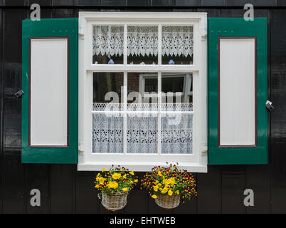 Fenster in ein schwarzes Holzhaus mit grünen und roten Fensterläden und zwei kleine Körbe mit Blumen in der Stadt von Marken, Holland Stockfoto