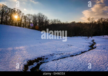 Sonnenuntergang über einem Bach in einem schneebedeckten Feld in ländlichen Baltimore County, Maryland. Stockfoto