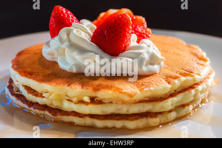 Drei amerikanische Pfannkuchen in einem Stapel mit Schlagsahne und Erdbeeren obendrauf. Stockfoto