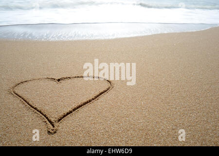 Liebe Herz gezeichnet in den Sand am Strand, mit einer Ozeanwelle rund um es abzuwaschen. Stockfoto