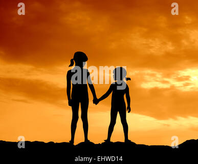 Silhouette der beiden Mädchen Hand in Hand gegen einen wunderschönen Sonnenuntergang Stockfoto