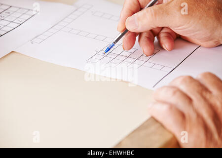 Hand des älteren Menschen mit Stift lösen Kreuzworträtsel für Gedächtnistraining Stockfoto