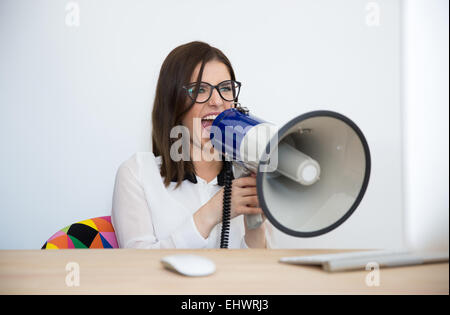 Geschäftsfrau, die am Tisch sitzen und sprechen über Megaphon Stockfoto