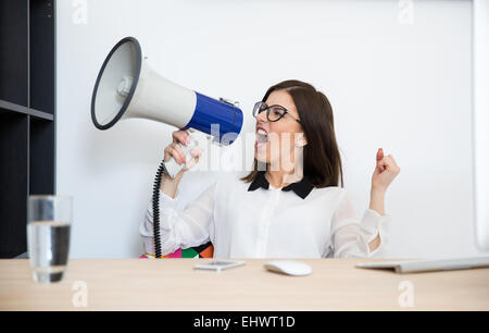 Geschäftsfrau, die am Tisch sitzen und sprechen über Megaphon Stockfoto