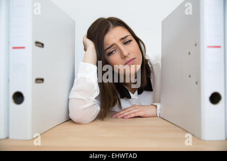 Müde Geschäftsfrau, die in der Tabelle mit Ordnern im Büro sitzen Stockfoto
