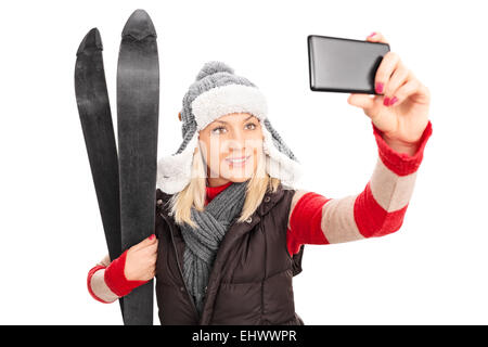 Frau hält ein paar Ski und ein Selbstporträt mit Handy isoliert auf weißem Hintergrund Stockfoto