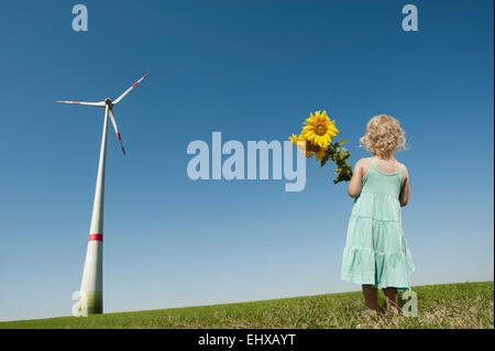 Mädchen halten Sonnenblumen in einem Windpark, Bayern, Deutschland Stockfoto