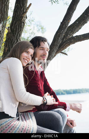 Glückliches junges Paar sitzt See Stockfoto