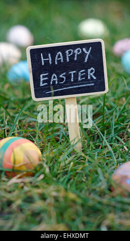 Frohe Ostern, geschrieben auf einer Tafel stehen im Rasen zwischen Ostereiern Stockfoto