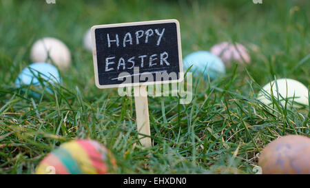 Frohe Ostern, geschrieben auf einer Tafel stehen im Rasen zwischen Ostereiern Stockfoto