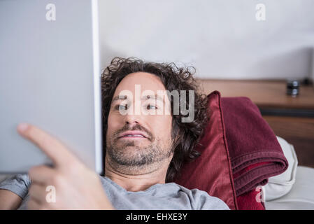 Mann auf der Couch liegend und mit Hilfe einer digitalen-Tablets, München, Bayern, Deutschland Stockfoto