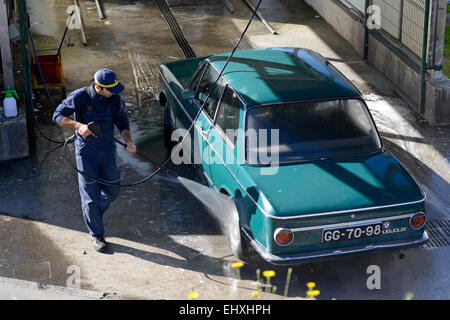 Junger Mann Waschen Auto mit Hochdruck-Wasserschlauch an eine professionelle Fahrzeugreinigung Stockfoto