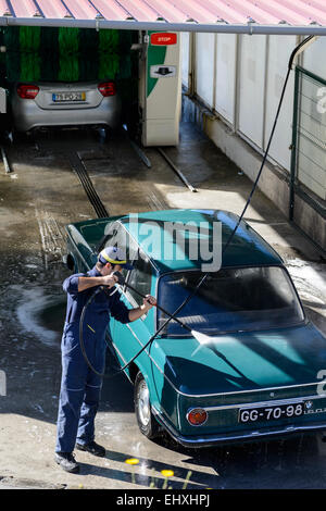 Junger Mann Waschen Auto mit Hochdruck-Wasserschlauch an eine professionelle Fahrzeugreinigung Stockfoto