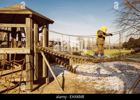 Kleinen Jungen zu Fuß entlang einer Hängebrücke auf einem Spielplatz Stockfoto