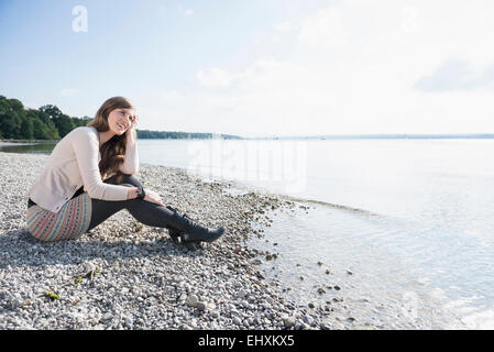 Hübsche junge Frau sitzt am Ufer Stockfoto