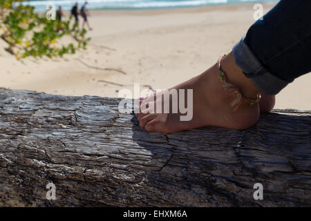 Eine Dame ruht ihre Füße auf ein zerklüfteter Baumstamm auf der schönen Strand Robberg Halbinsel, Südafrika Stockfoto