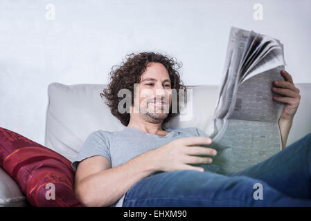 Mann, liegend auf der Couch und liest eine Zeitung, München, Bayern, Deutschland Stockfoto