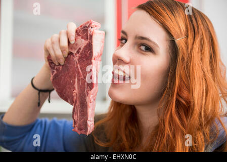 Junge Frau hält eine Scheibe Schinken und leckte ihre Lippen auf verführerische Weise, München, Bayern, Deutschland Stockfoto