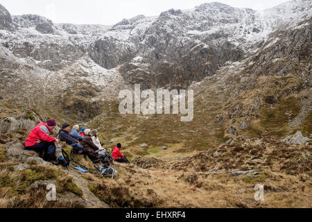 Gruppe der Wanderer eine Pause in Cwm Clyd mit Schnee auf Y Garn Berg jenseits in Snowdonia. Ogwen, Gwynedd, Nordwales, UK Stockfoto