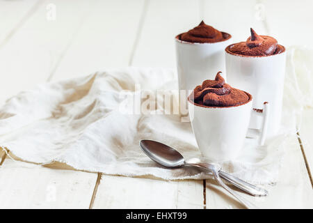 Drei Tassen vegane Mousse au Chocolat, Teelöffel, Tuch auf weißem Holz Stockfoto