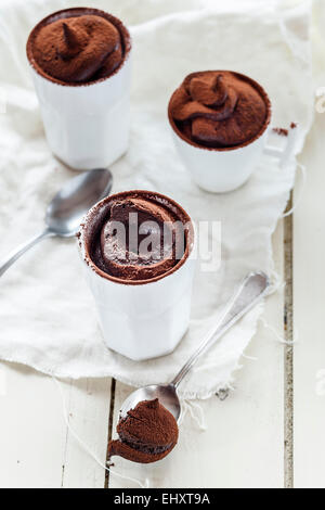 Drei Tassen vegane Mousse au Chocolat, Teelöffel, Tuch auf weißem Holz Stockfoto